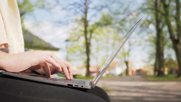 Close up hands of woman sitting on a chair and spending time to work on laptop at park