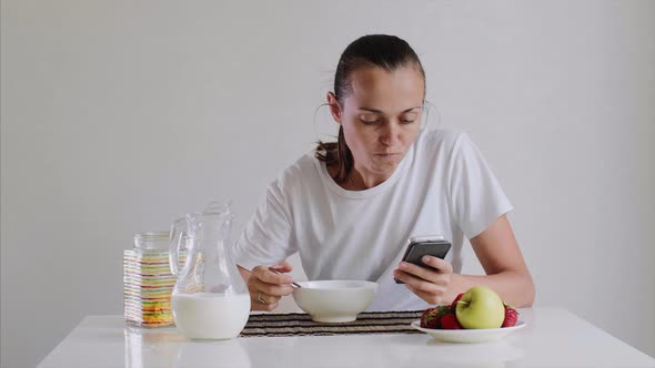 Young Woman Is Having a Breakfast and Looking in Smartphone.