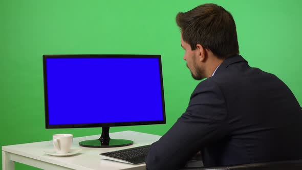 A Young Businessman Sits at a Desk and Looks at a Desktop Computer - Green Screen Studio alt