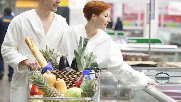 Young Couple in Bathrobes in Supermarket Doing Daily Shopping Walking with Cart