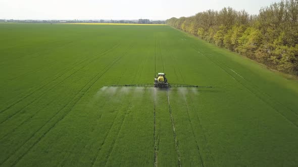 Aerial view of a tractor spraying chemical pesticides with sprayer on the large green field  alt