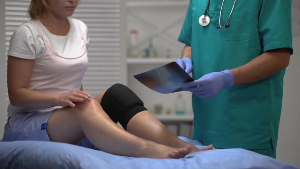 Physician Explaining Broken Leg Bone X-Ray to Female in Neoprene Knee Brace