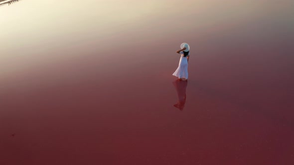 Beautiful Woman in a White Dress Walking on a Pink Lake at Sunset alt
