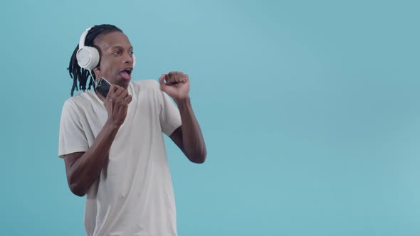 Black Man Listens to Music with Headphones and Holding a Phone in Hand Emotionally Dancing Smiling alt