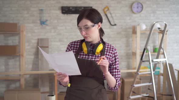 Portrait Professional Young Worker Carpenter Woman with Drawings in Hand alt