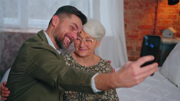 Millennial Son and His Elderly Mother Taking a Selfie with a Smartphone Celebration of Mother's Day alt