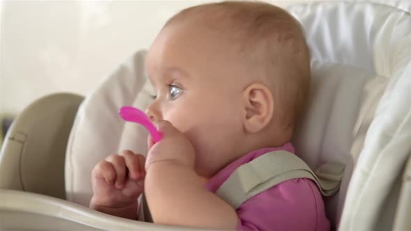 Little cute girl sits behind a children's chair and plays with spoon. Close-up. alt
