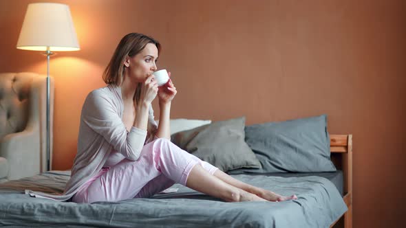 Happy Relaxed Barefoot Young Woman Drinking Hot Tea in Bedroom Enjoying Weekend at Home alt