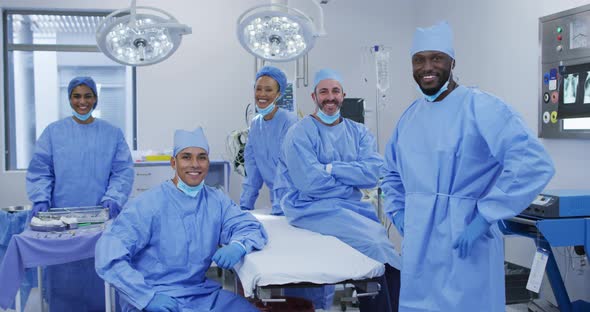 Diverse male and female doctors wearing face masks standing in operating theatre smiling to camera alt