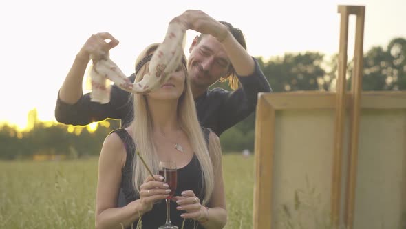 Brunette Man Opening Woman's Eyes and Showing Picture. Portrait of Loving Husband Presenting alt