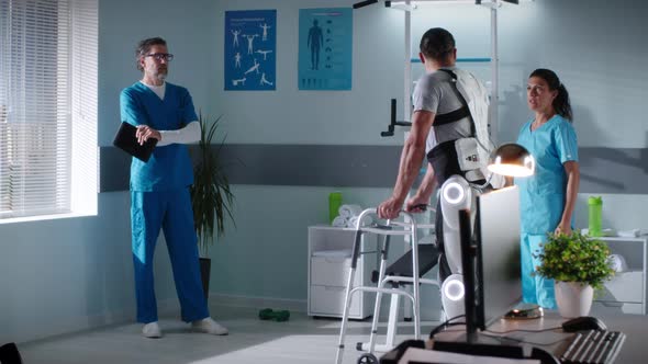 Doctors Discussing Rehabilitation Progress of Man Strolling with Walking Frame alt