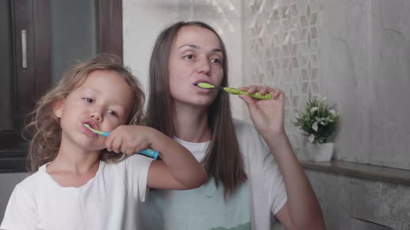 Mom and Her Cute Little Daughter is Brushing Teeth with Toothbrushes Together