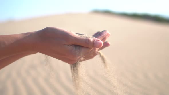 Close up of woman pouring sand running through fingers slow motion at the beach with sun flare 