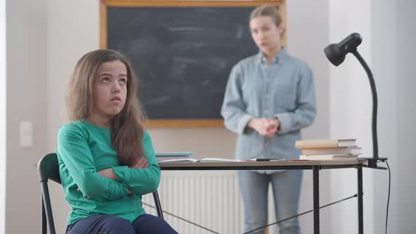 Portrait of Young Stubborn Little Woman with Crossed Hands Rolling Eyes As Blurred Teacher Talking alt