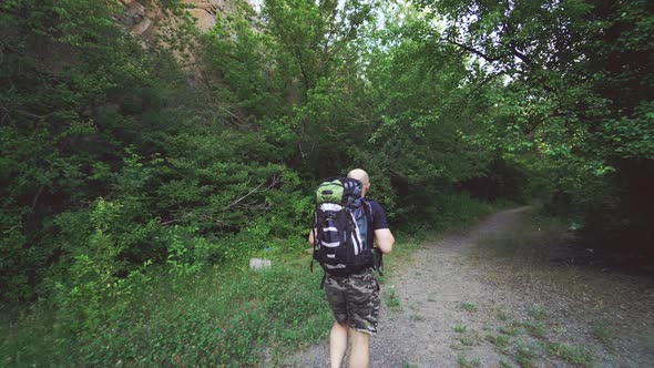 tourist with a backpack in shorts and a t-shirt is going along a path in the forest alt
