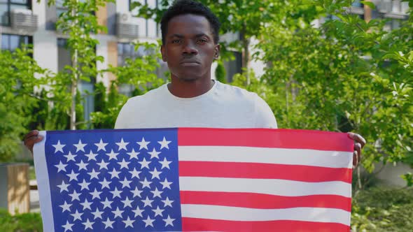 Portrait Afroamerican Man Holding an American Flag and Looks Camera in Summer alt