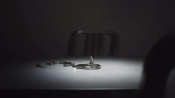 Medium tracking shot of a pair of handcuffs on a table in an interrogation room. alt