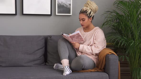 Young Female Writing in Notebook While Sitting on Comfortable Couch at Home