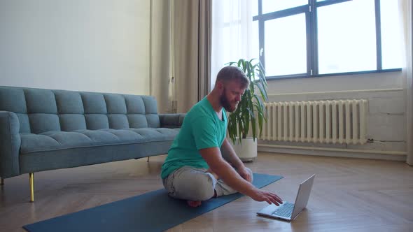 Middleaged Man Taking an Online Yoga Class  He Meditating on the Floor in Front of a Laptop Monitor alt
