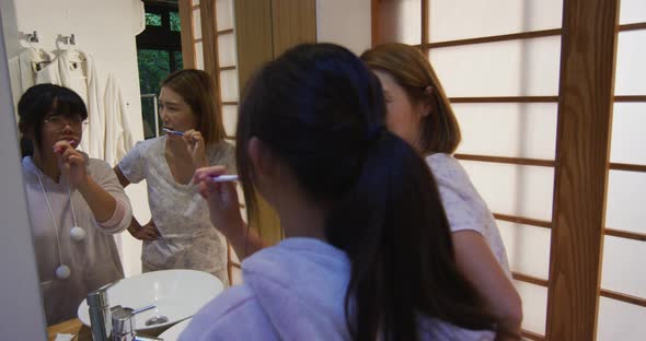 Asian mother and daughter standing in bathroom and brushing teeth alt