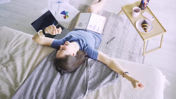 Young Woman with Pad Sits on Floor Leaning on Bed By Table