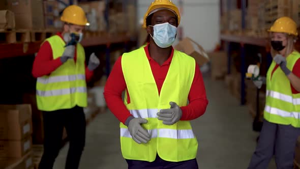 Happy multiracial staff dancing in warehouse while wearing protective face masks for coronavirus