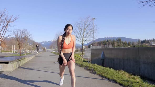 Latina Runner Stops to Catch Breath with Hands on Knees in Orange Sports Bra alt