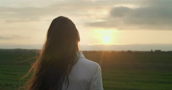 Back Portrait of Long-haired Girl Stroking Hair on Country Sunset Background Copy Text Space