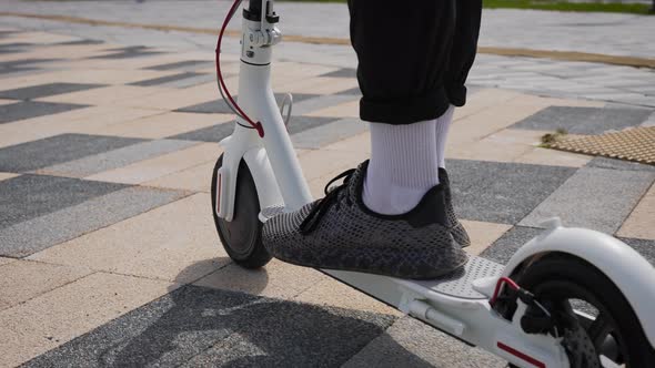 Men's Feet in Sneakers on an Electric Scooter alt