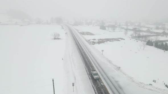 Snow storm in rural Wisconsin valley with poor visibility on a recently plowed highway.