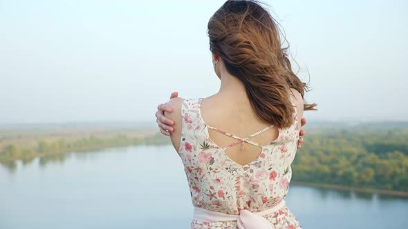 Attractive Woman with Loose Hair Hugs Shoulders on Riverbank alt