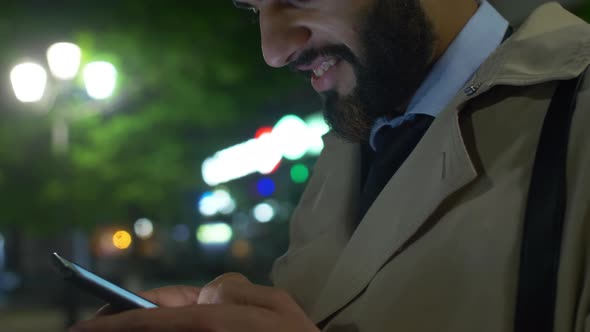 Smiling Middle Eastern man texting on smartphone alt
