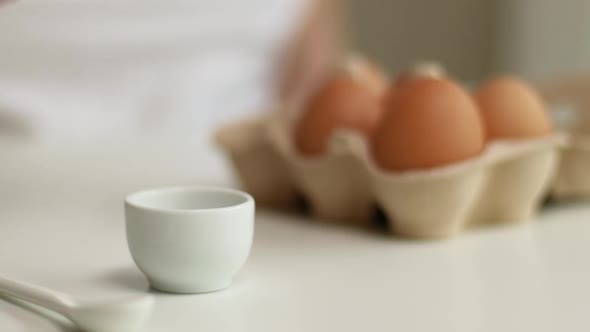 Person Hand Takes Boiled Egg From Egg Cup on White Table