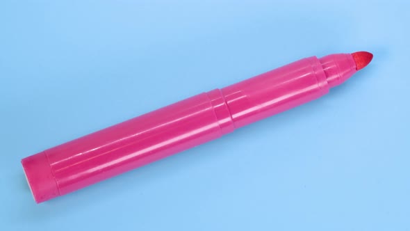 Pink marker pen rotating on blue surface background, macro shot close up view detail. alt