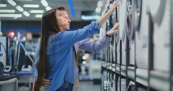 Young Man and Woman in Appliances Store Choose To Buy Washing Machine for Home. Open the Door alt
