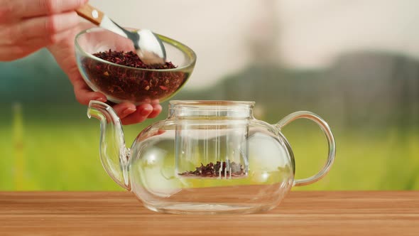 Putting Dry Tea Leaves Into Teapot on a Wooden Table alt