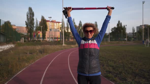 Senior Woman Stretching Before Nordic Walk with Hiking Poles on Running Track of Stadium alt
