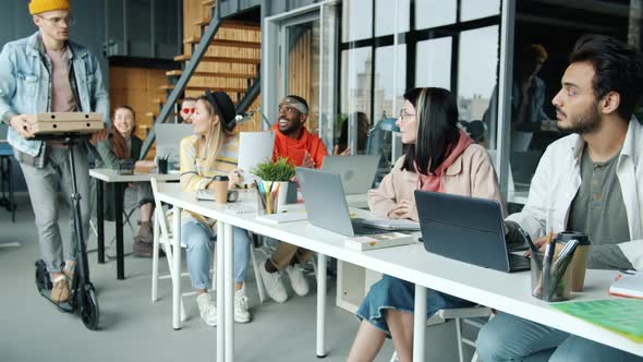 Businessman Bringing Takeaway Pizza to Office Riding Scooter Inviting Colleagues to Lunch alt