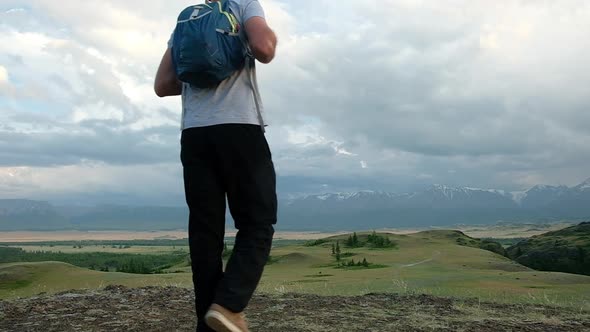 traveler walks through hills of mountain valley with a backpack on his shoulders