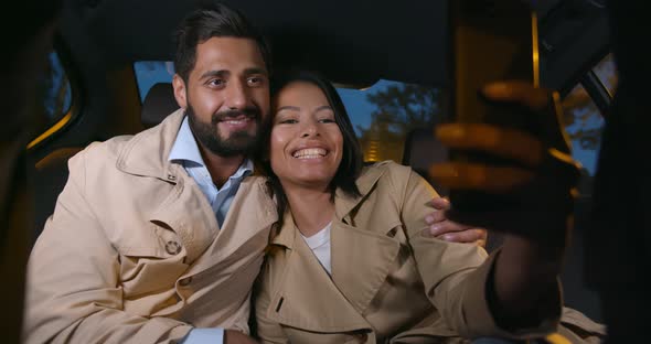 Happy Couple Smiling in Backseat of Car Taking Selfie on Smartphone alt