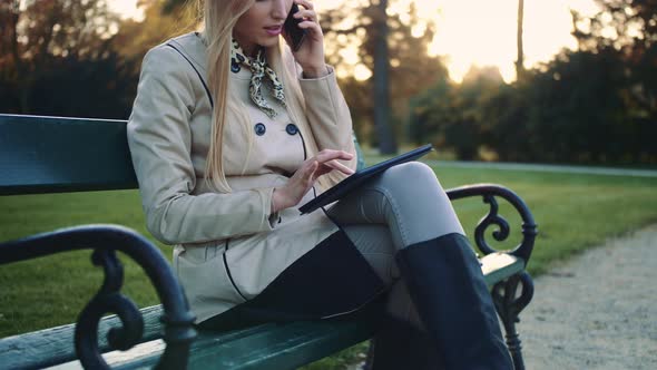 Beautiful Girl on a Bench with Tablet Computer and Cellphone Sitting on Park Bench alt
