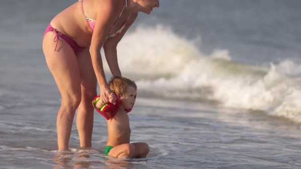 Mom Plays with the Baby in Oversleeves Throwing Him Over the Waves on a Summer Evening alt