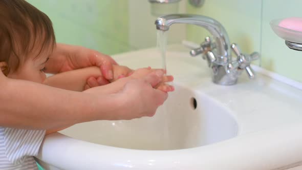 Mom washes her baby's hands in the bathroom. alt