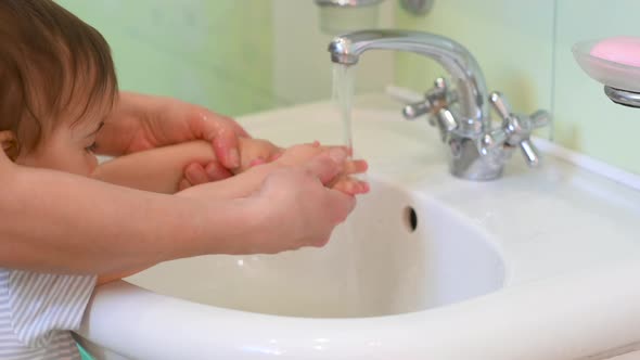 Mom washes her baby's hands in the bathroom.