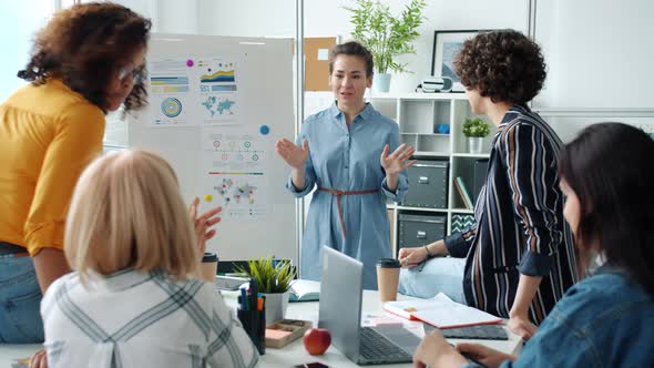 Cheerful Young Businesswoman Giving Good News To Colleagues Making Report with Board in Office alt