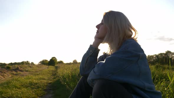 beautiful blond hair girl is sitting on countryside road during sunset