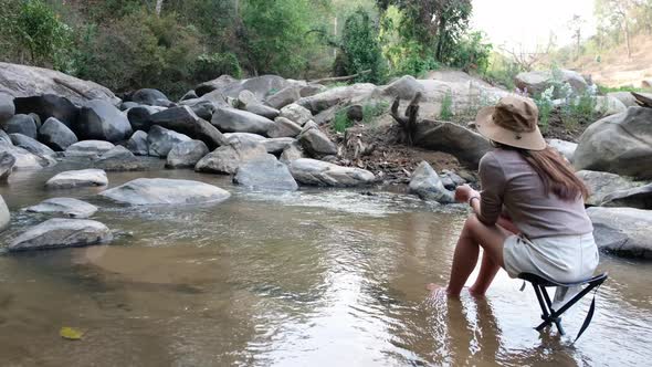 Rear view of a young Asian woman sitting and relaxing on a chair in waterfall stream