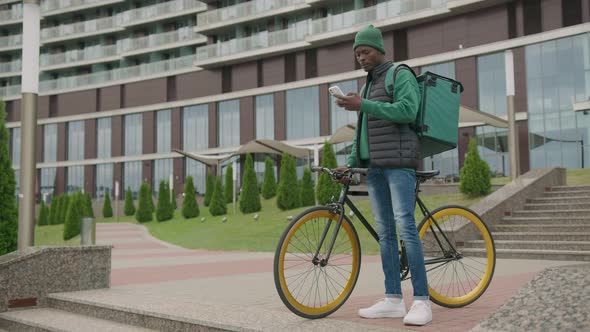 young african man works as a food delivery man. sitting on a bench in a smartphone.