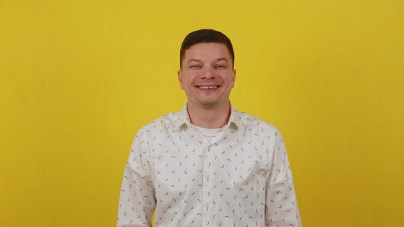 Happy Smiling Guy 20 Years Old in a White Shirt Shows Thumbs Up on a Yellow Background alt