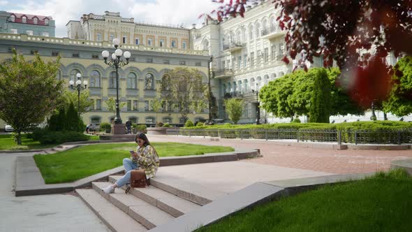 A Young Girl is Sitting in the Park and Texting on the Phone